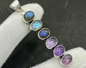 May include: A silver pendant featuring a series of oval-shaped gemstones. The gemstones include blue labradorite and purple amethyst, set in individual bezels. The pendant has a loop at the top for a chain.