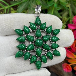 May include: A silver pendant featuring a starburst design with green malachite gemstones. The pendant has a detailed silver bail and is composed of teardrop and round-shaped stones. The malachite has a distinctive green color with darker green veining.