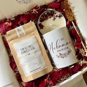 Könnte beinhalten: Eine weiße Geschenkbox gefüllt mit roten Rosenblättern, eine weiße Tasse mit dem Text "Beste Hebamme Danke für alles", ein brauner Teebeutel mit dem Text "Ein kleines Dankeschön" und eine weiße Kerze mit roten Rosenblättern darauf.