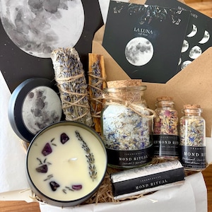 Könnte beinhalten: Ein Ritual-Geschenkset mit einer Kerze in einer schwarzen Dose, verziert mit Amethyst und Lavendel, einem Lavendelbündel, einem Palo Santo-Stab, drei Glasfläschchen mit botanischen Salzen und Mondkarten mit der Aufschrift LA LUNA.