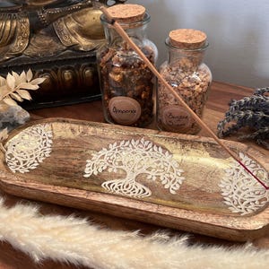 Könnte beinhalten: Ein Holz-Räucherofen mit einem Lebensbaum-Design. Der Räucherofen ist mit Blattgold verziert und hat zwei kleine Glasgefäße mit Korkdeckeln. Die Gefäße sind mit "Opoponax" und "Benzoin Siam" beschriftet.