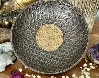 May include: A dark brown wooden bowl with a geometric pattern and a gold flower of life design in the centre.