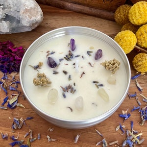 Könnte beinhalten: Eine weiße Kerze mit einem silbernen Deckel, in die kleine violette und weiße Kristalle sowie getrocknete Lavendelblüten eingebettet sind.
