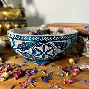 Könnte beinhalten: Eine blaue und weiße geschnitzte Steinschale mit einem Lebensblume-Design. Die Schale ist mit getrockneten Kräutern und Blumen gefüllt.