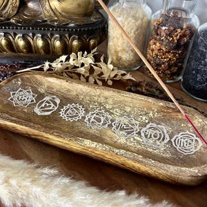 Könnte beinhalten: Ein Holz-Räucherofen mit goldenen Akzenten und sieben Chakra-Symbolen. Der Ofen ist mit einem roten Räucherstäbchen gefüllt.