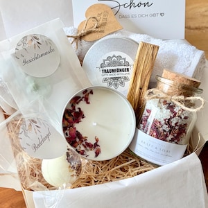 Könnte beinhalten: Eine Geschenkbox mit einem weißen Handtuch, einer Kerze in einer silbernen Dose mit getrockneten Rosenblättern, einem Glas mit Korken gefüllt mit Badesalz und getrockneten Blüten, einer Badekugel, einer Gesichtsmaske und einem Holzherz.