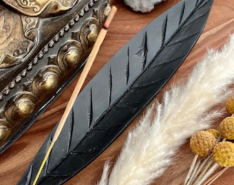 Könnte beinhalten: Schwarzer, blattförmiger Räucherofen aus Holz mit geschnitztem Design. Ein Holzstäbchen-Räucherwerk ist auf dem Räucherofen platziert.