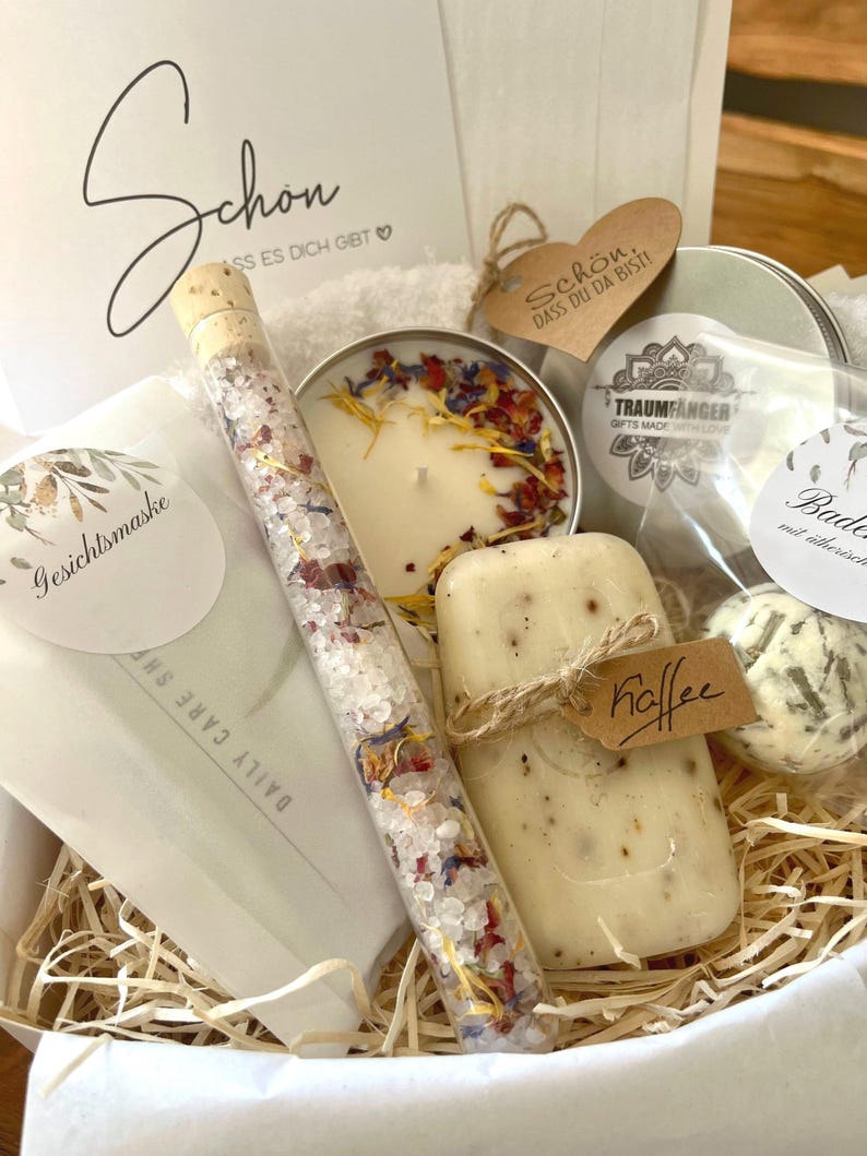 May include: A gift basket filled with bath and body products. The basket includes a candle, bath salts, soap, and a bath bomb. The basket is decorated with a tag that says "Sch&ouml;n. Dass du da bist!" which translates to "Beautiful. That you are here!"
