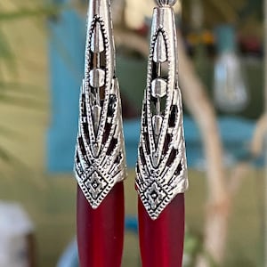 May include: A pair of silver dangle earrings with red glass teardrop-shaped stones. The earrings have a detailed filigree design.