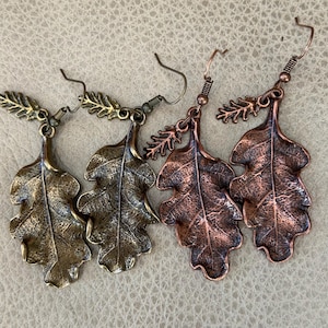 May include: Four pairs of leaf-shaped earrings in bronze and copper tones. Each earring has a detailed oak leaf design with a small sprig detail. The earrings have a hook closure.