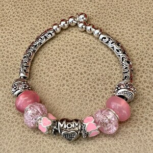 May include: A silver charm bracelet with pink beads and a heart charm that says "Mom Me".