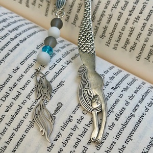 May include: Silver mermaid bookmark with a beaded chain featuring white, gray, and blue beads. The mermaid is curled in a wave-like shape with a detailed design.
