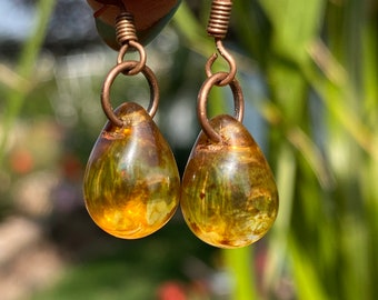 May include: A pair of teardrop-shaped earrings with a copper wire hook and a translucent amber-colored glass bead. The beads have a swirling pattern of gold and green.