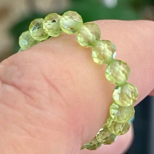 Puede incluir: Un brazalete de piedras preciosas verdes hecho de cuentas facetadas. El brazalete está hecho de muchas cuentas pequeñas y redondas que se ensartan para formar un círculo.