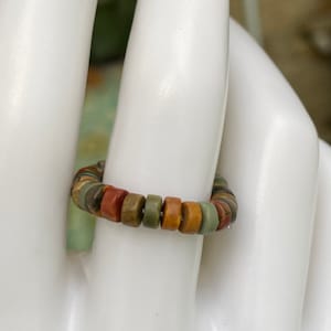 Puede incluir: Un anillo hecho de cuentas redondas de piedra de colores. Las cuentas son en tonos de verde, marrón y rojo.