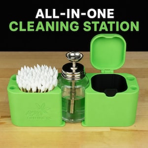 May include: A green all-in-one cleaning station with the text "ALL-IN-ONE CLEANING STATION". The station includes a container of cotton swabs, a glass bottle, and a compartment with a lid. The station is on a wooden surface.
