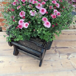 May include: A wooden planter shaped like a chair, stained black. The planter is filled with pink chrysanthemums.