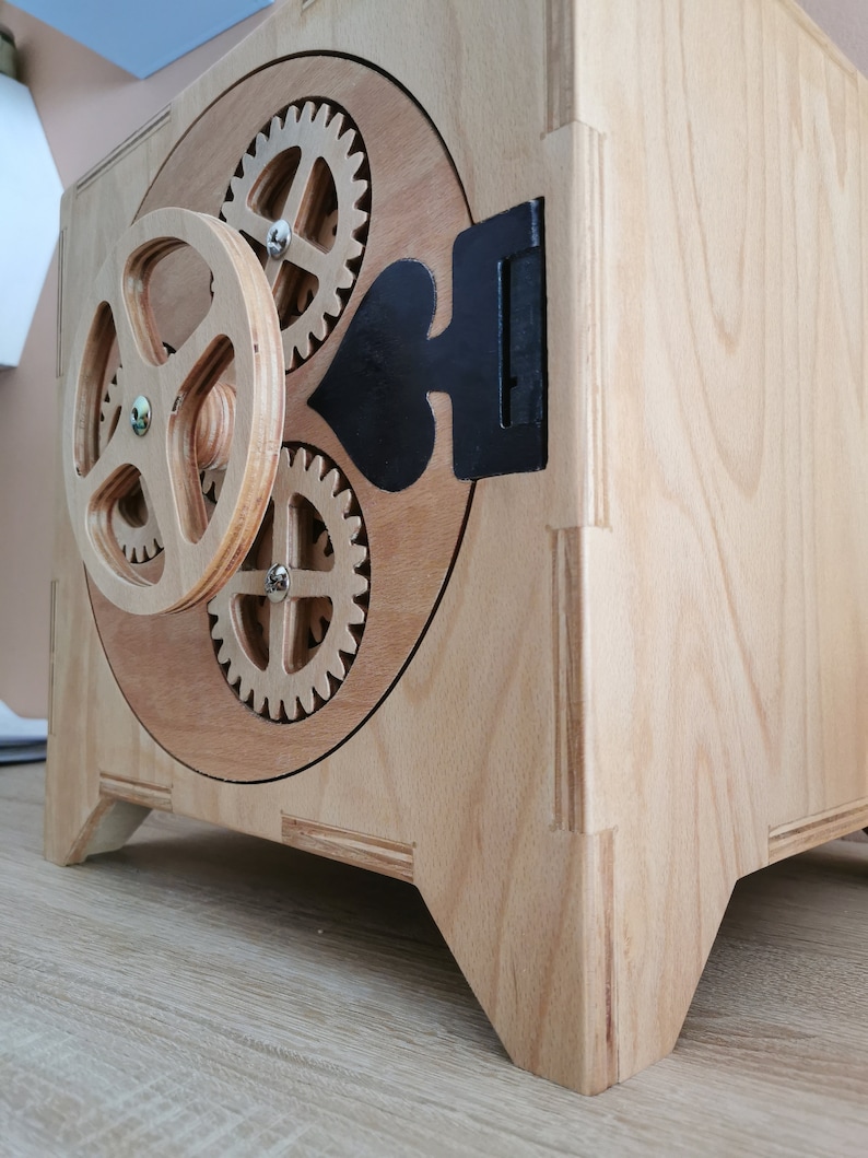 May include: A wooden box with a hinged door and a gear mechanism. The door has a black heart shape cutout and a black metal hinge. The box has four legs.