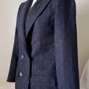 May include: A dark blue blazer with a subtle silver pattern. The blazer has a double-breasted closure with two buttons and a single pocket on the left side.