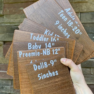 May include: A set of wooden size guides for different ages, including adult, teen, kid, toddler, baby, preemie, and doll. The guides are labeled with the age range and corresponding measurements in inches.