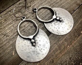 May include: A pair of silver earrings with a hammered texture and a circle design. Each earring has a small circle with a bead detail.