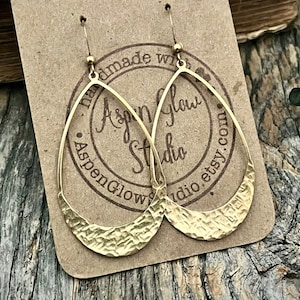 May include: Gold hammered teardrop earrings with a textured finish. The earrings are hanging on a brown card with the text "Aspen Glow Studio" and "AspenGlowStudio.etsy.com".