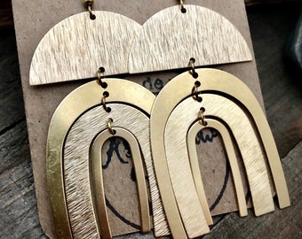 May include: Gold tone earrings with a layered arch design. The earrings are made of brushed metal and have a modern, geometric look.