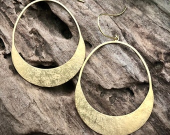May include: A pair of gold hoop earrings with a textured finish. The earrings are large and have a crescent moon shape.