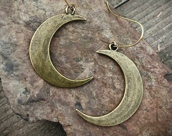 Könnte beinhalten: Ein Paar goldene Halbmond-Ohrringe. Die Ohrringe sind aus Metall und haben ein schlichtes, elegantes Design.