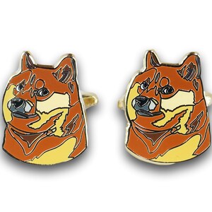 以下が含まれることがあります： 茶色、オレンジ、黄色のデザインの柴犬が描かれた、ゴールドトーンのカフスボタンのペアです。