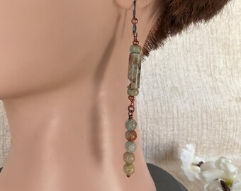 Peut inclure: Longues boucles d'oreilles pendantes aux tons terreux. Les boucles d'oreilles ont un crochet en métal foncé, avec une série de perles dans les tons de vert, de marron et de beige. Le design comprend une pierre rectangulaire et des perles rondes.