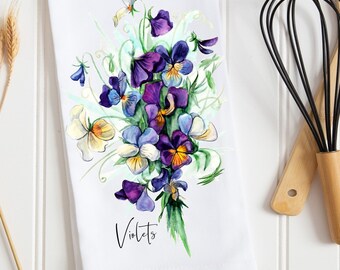 Op de afbeelding: Een witte keukendoek met een aquarel-illustratie van een boeket paarse, gele en witte viooltjes. De tekst "Violets" is onder de bloemen gedrukt.