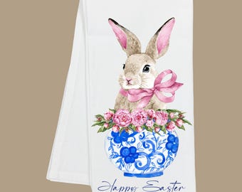 May include: White Easter-themed kitchen towel with a watercolour illustration of a bunny wearing a pink bow, above a blue and white floral vase filled with pink flowers. The words "Happy Easter" are written in script.