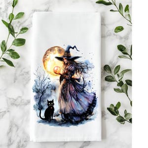 May include: White cotton kitchen towel featuring a watercolor illustration of a witch in a long dress and hat, holding a glowing orb. A black cat sits nearby, with a full moon in the background. The design has a Halloween theme.
