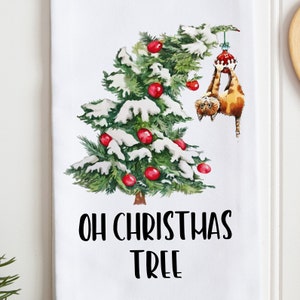 Könnte beinhalten: Ein weißes Geschirrtuch mit einer Aquarell-Illustration eines Weihnachtsbaums mit roten Kugeln und Schnee. Eine Katze hängt kopfüber am Baum und hält eine rote Kugel fest. Der Text "OH CHRISTMAS TREE" ist unter dem Baum gedruckt.