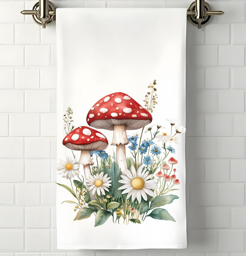 Op de afbeelding: Een witte keukendoek met een aquarel-illustratie van rode en witte paddenstoelen en blauwe en witte bloemen.