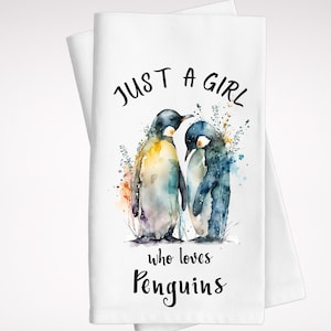 May include: A white tea towel with a watercolor illustration of two penguins. The text "JUST A GIRL who loves PENGUINS" is printed in black.