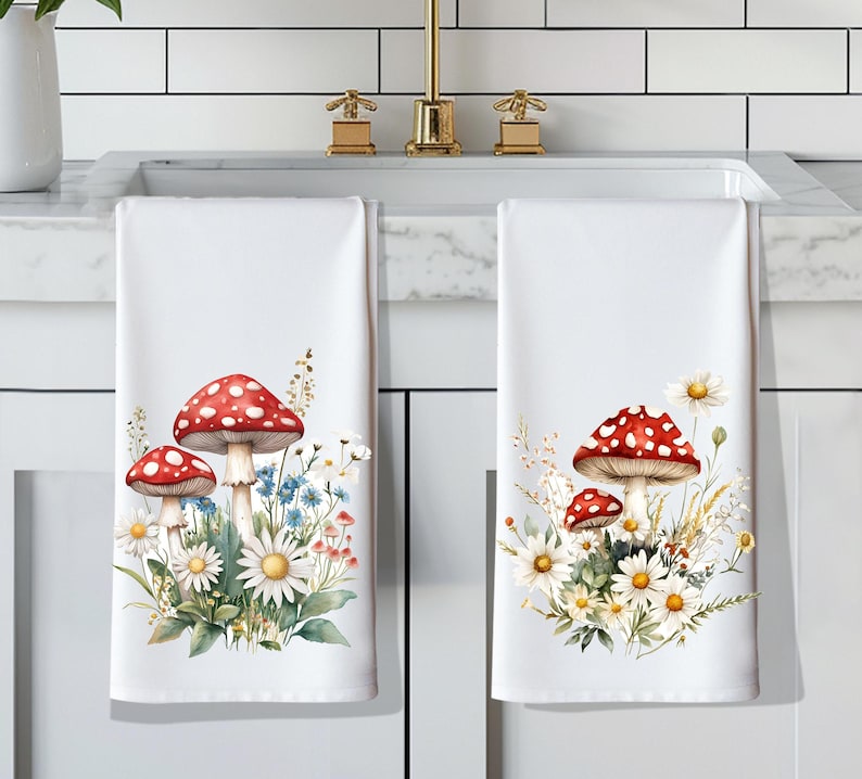 Op de afbeelding: Twee witte keukendoeken met een rood en wit paddenstoel- en madeliefjesbloemendesign.