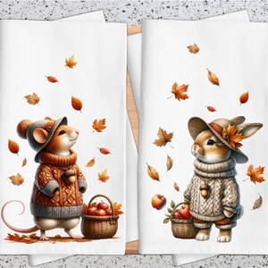 May include: Two kitchen towels with autumn-themed illustrations. The first towel features a brown mouse wearing a knitted sweater and a hat, holding a basket of apples. The second towel features a brown rabbit wearing a knitted sweater and a hat, holding a basket of apples. Both towels have a white background with falling autumn leaves.