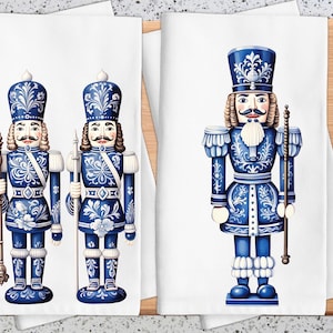 May include: White kitchen towels with blue and white nutcracker soldier designs. The nutcrackers have ornate uniforms and moustaches, holding staffs. The towels are displayed on a wooden chopping board.