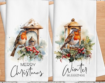 May include: Two white kitchen towels with watercolor illustrations of robins perched on birdhouses, surrounded by holly and berries. One towel reads "MERRY Christmas," the other "WINTER BLESSINGS."