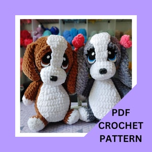 May include: PDF crochet pattern for two amigurumi dogs. One dog is brown and white, the other is gray and white. Both dogs have big eyes and are sitting.