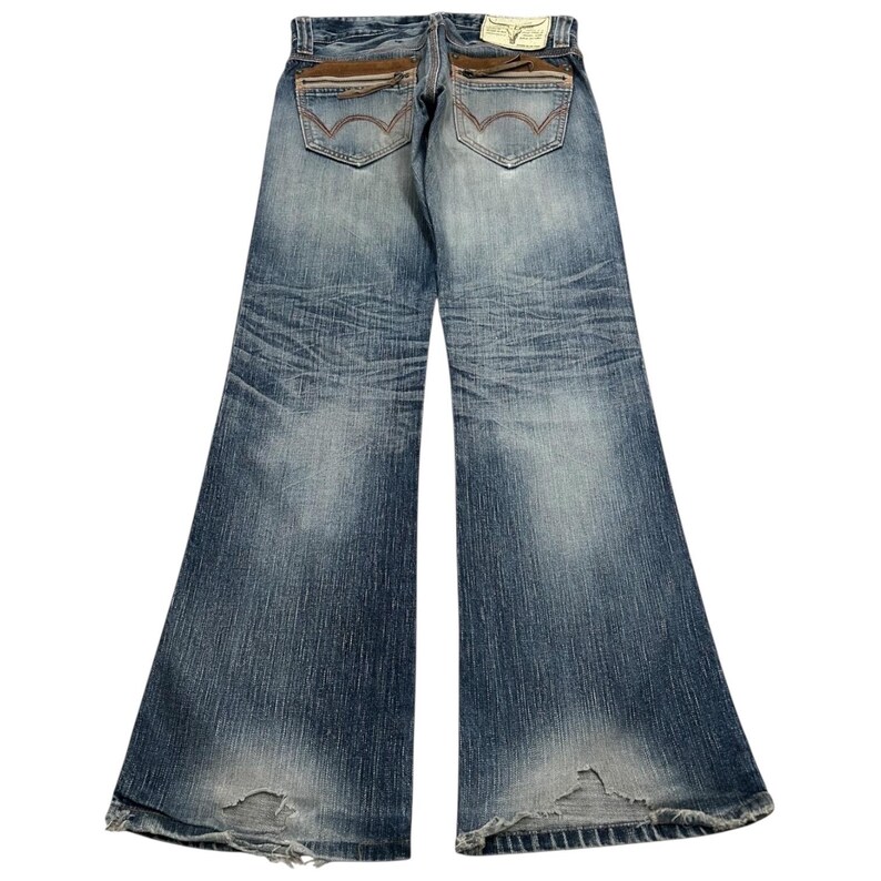 May include: Faded blue denim jeans with a wide leg design. The jeans feature brown suede-like accents on the back pockets and a distressed look at the hem. A small tag is visible at the back of the waistband.