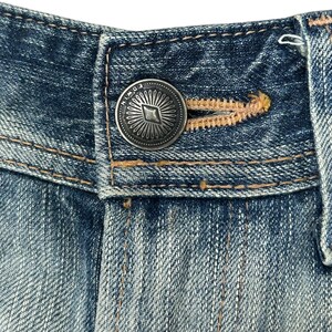 May include: Close-up of a denim jeans waistband featuring a silver button. The button is embossed with the brand name "EDWIN" and a sunburst design. The jeans show visible stitching and a buttonhole.