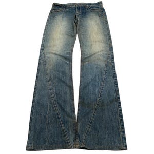 May include: Light blue denim jeans with a flared leg design. The jeans have a faded wash and feature decorative stitching around the pockets and waist. The jeans are laid flat, showcasing the full length and details.