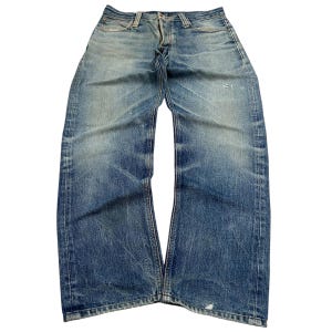 Puede incluir: Vaqueros de mezclilla azul descolorido con un diseño clásico de cinco bolsillos. Los vaqueros muestran signos de desgaste, incluyendo áreas desgastadas y decoloración, dándoles un aspecto vintage. Los vaqueros están planos, mostrando toda la longitud y los detalles.