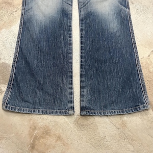 May include: A pair of blue denim jeans with a flared leg design. The jeans have a faded wash effect and visible stitching along the seams. The bottom hem is finished with a classic rolled edge.