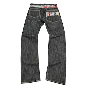 May include: Dark grey denim jeans with decorative floral fabric on the back pockets and waistband. The jeans have a straight leg cut and white stitching. The back pockets are rectangular.