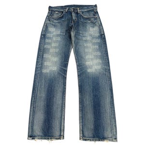 以下が含まれることがあります： 色あせたブルーデニムのジーンズ。ダメージ加工が施されています。ジーンズは、クラシックな5ポケットのデザイン、ボタンとジッパーの留め具、ストレートレッグフィットです。デニムは、色あせたパッチで使い古された外観をしています。