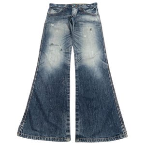 May include: Faded blue denim jeans with a wide, flared leg design. The jeans have a distressed look with intentional rips and fading. Classic five-pocket style with a button and zipper closure. The jeans are laid flat against a white background.